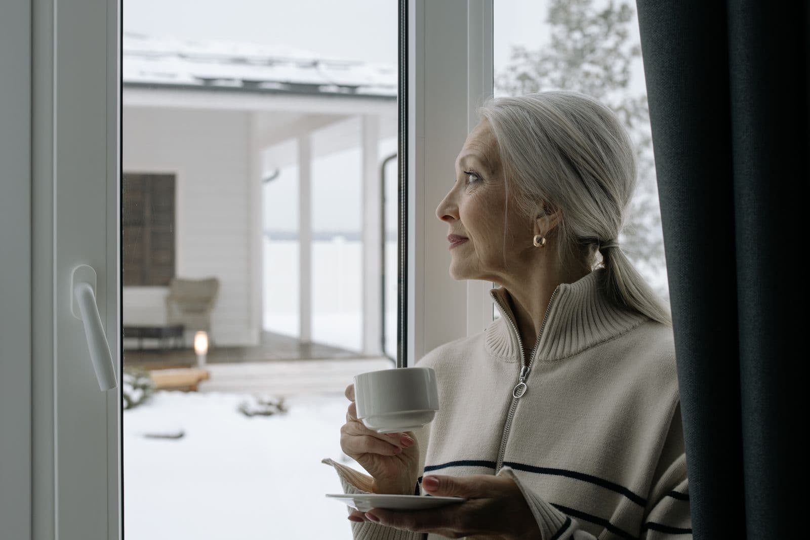 Mujer con una taza mirando por una ventana con nieve en el exterior