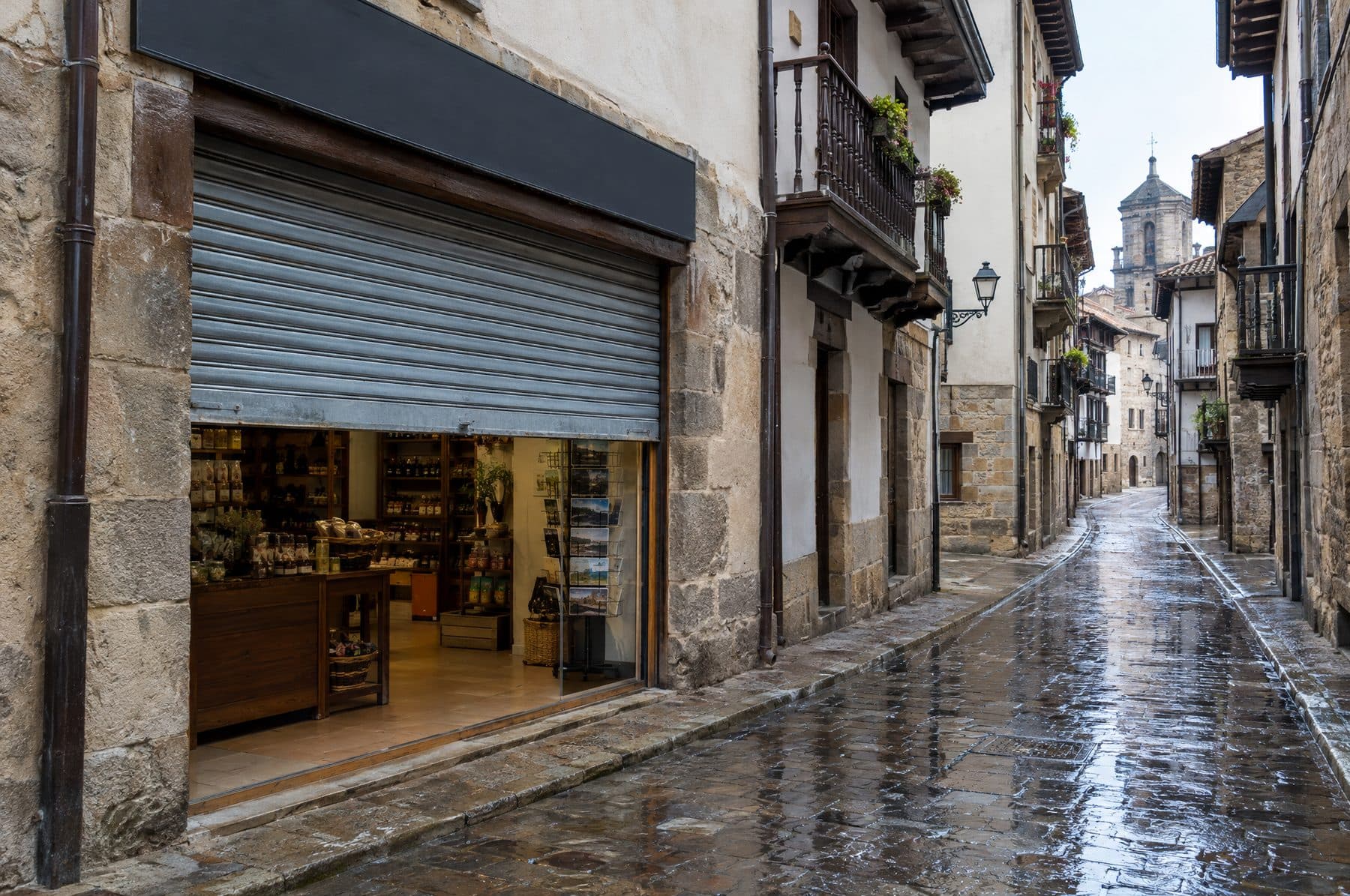 Cierre metálico de un comercio medio subido en una calle empedrada y mojada de un casco antiguo