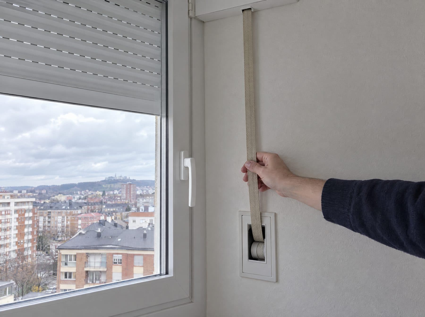 Cinta de persiana nueva que baja desde el cajón hasta un recogedor empotrado en la pared junto a la ventana