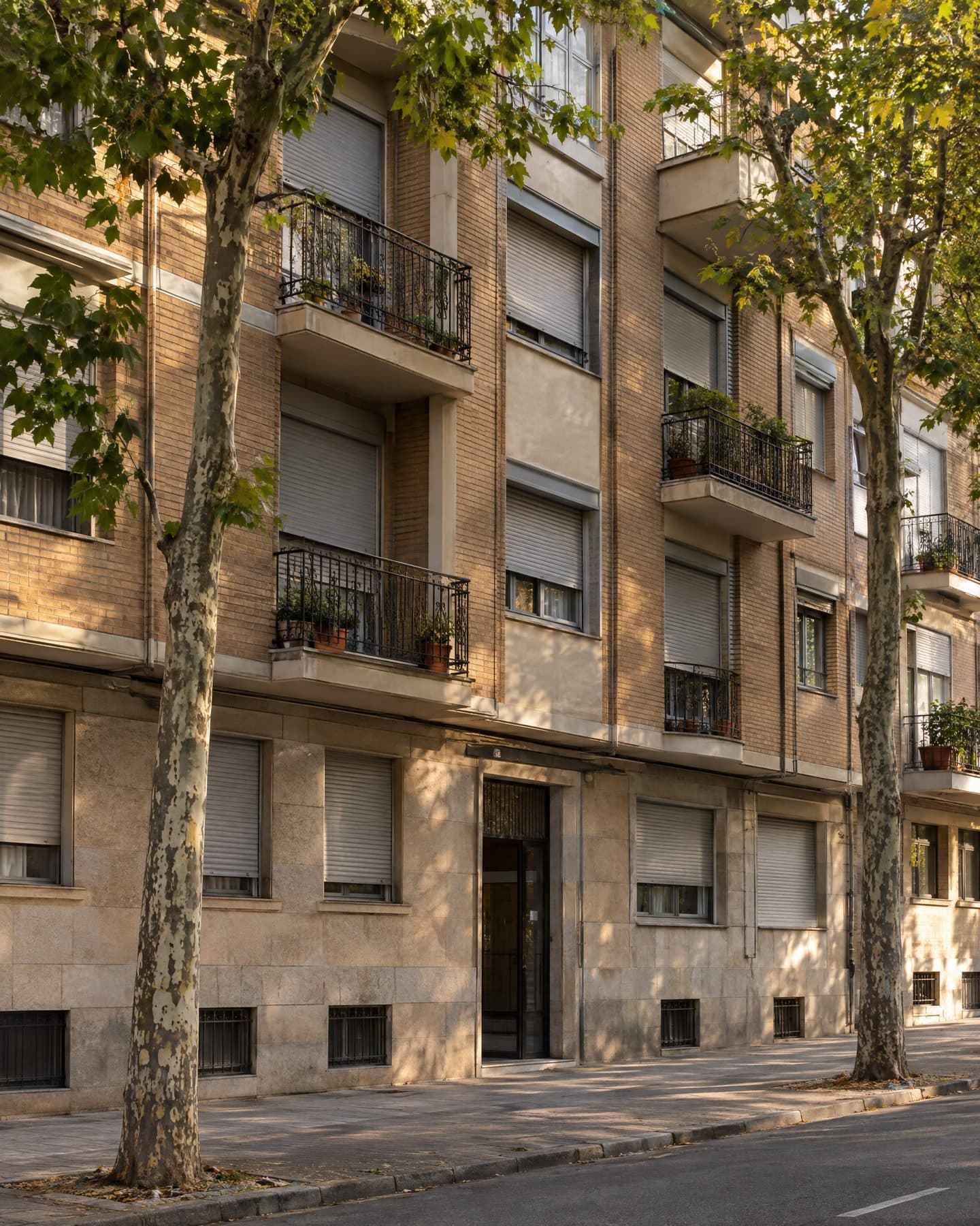 Fachada de un edificio de viviendas de ladrillo y piedra con balcones de forja y persianas grises bajadas a distintas alturas