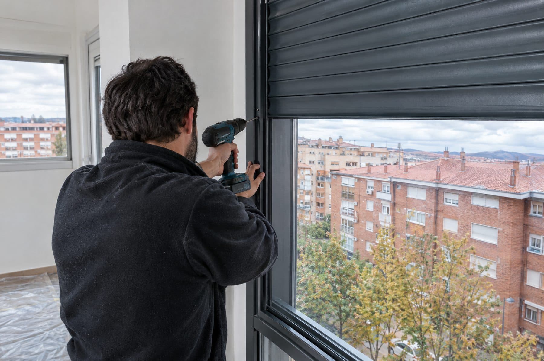 Instalador fijando con taladro la guía de una persiana de aluminio gris antracita nueva en una ventana