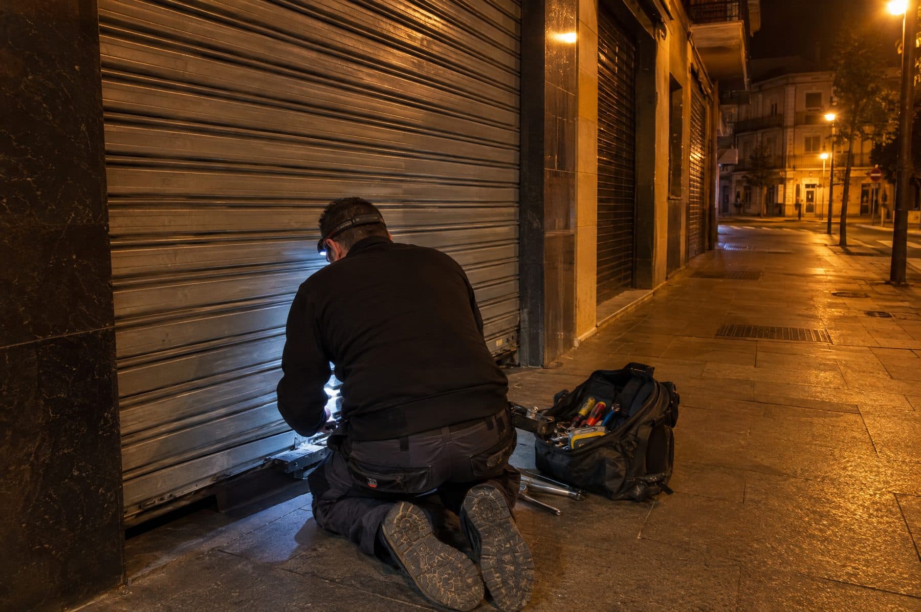 Técnico con linterna frontal reparando de noche la parte baja del cierre metálico de un local